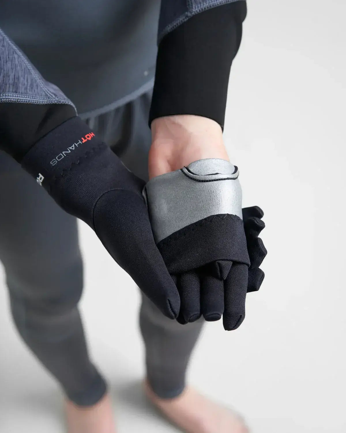 Sous gants néoprène 0.5mm tenus dans une main, montrant leur design technique et minimaliste.