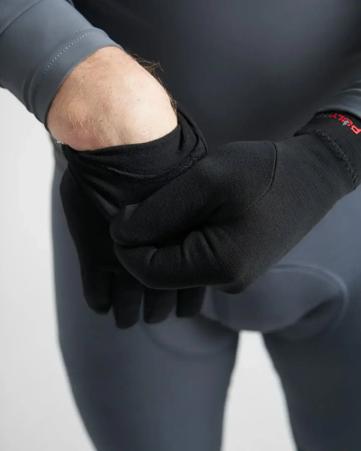 Gants PolyPro Liner en train d'être enfilés par un utilisateur dans une combinaison de plongée grise.