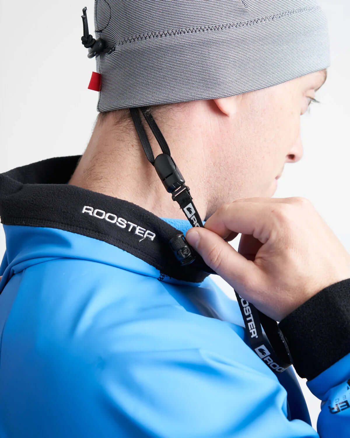Person adjusting the Leash casquette in a Rooster jacket with a focus on secure fastening.