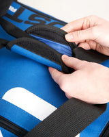 Détail du sac multifonctions 60L montrant une main ouvrant la poche avec fermeture éclair.